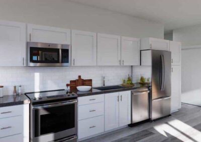 A modern kitchen with white cabinets, stainless steel appliances including a refrigerator, oven, and microwave, and a gray countertop. The backsplash features white subway tiles, and the floor is covered with light gray tiles.