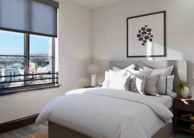 A modern bedroom with a large window showcasing a city view. The room features a neatly made bed with white linens and black and white accent pillows, flanked by wooden nightstands with lamps. A simple black and white artwork hangs above the bed.