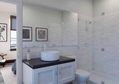 A modern bathroom features white subway tile walls, a white vanity with a black countertop, a round vessel sink, and a large mirror. To the left, a glimpse of a bedroom with a chair, framed artwork, and a potted plant is visible through an open door.